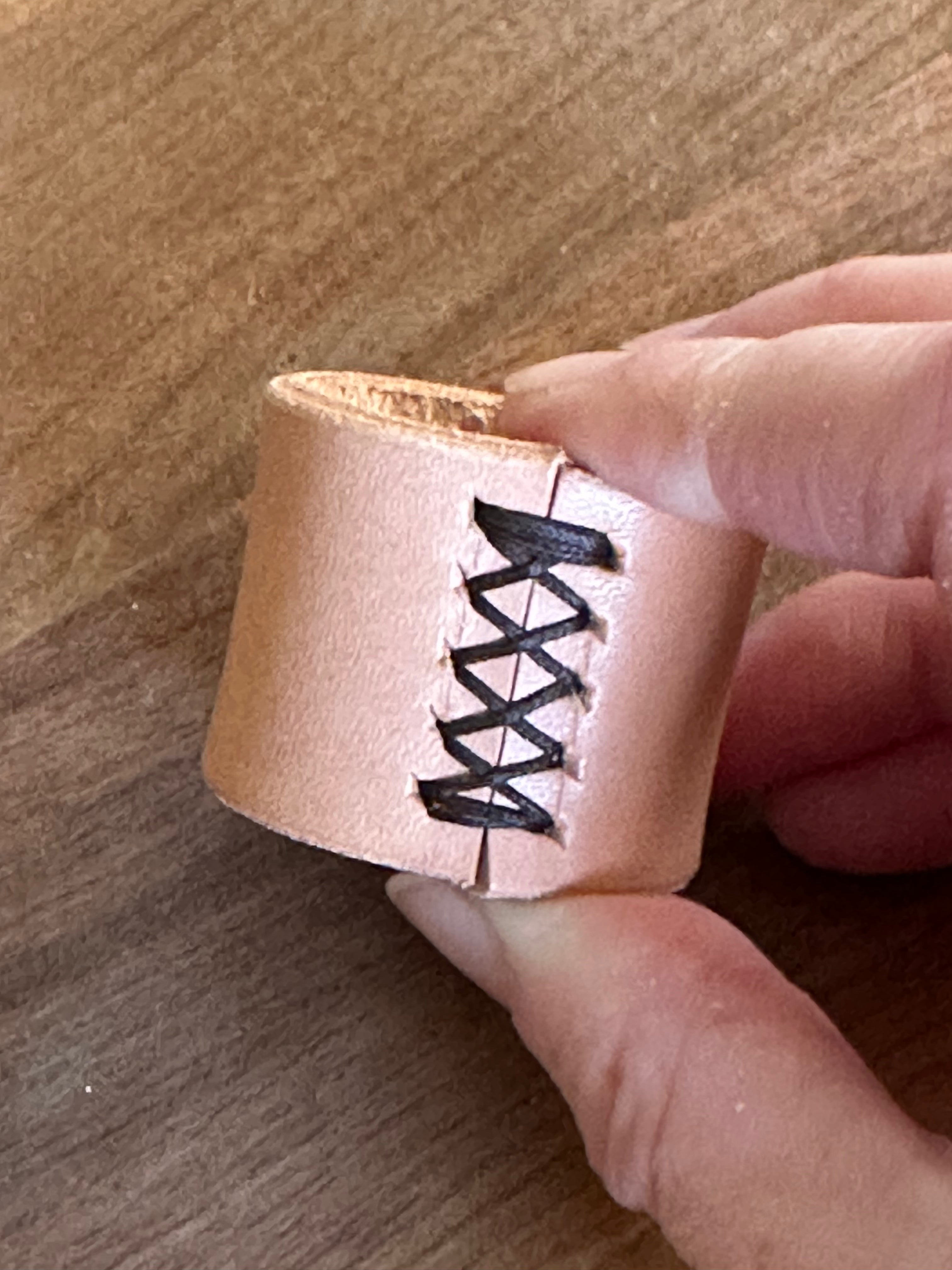 Hand holding a pink leather cuff with black stitching on a wooden surface