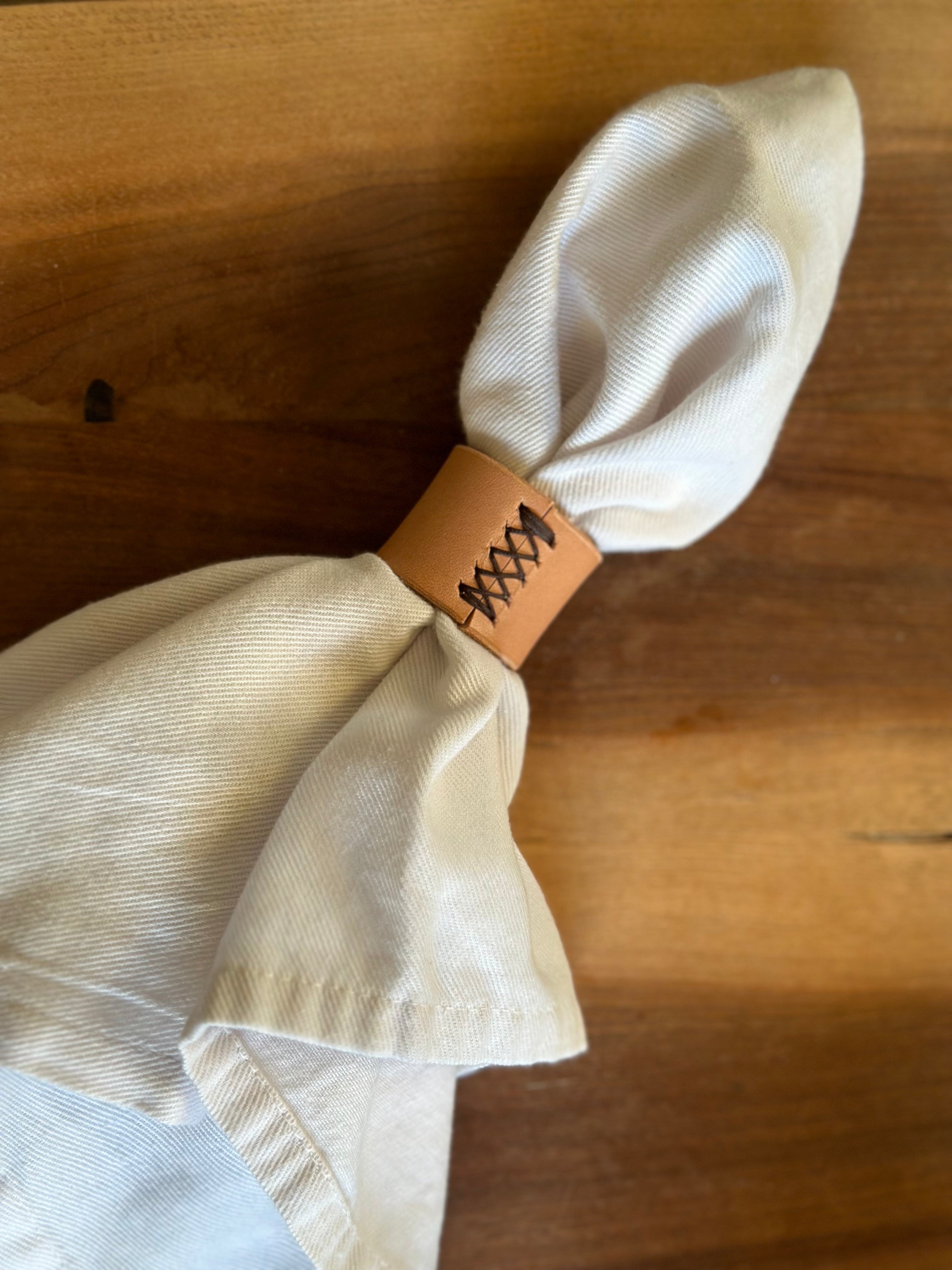 Beige napkin tied with a brown leather tie on a wooden surface